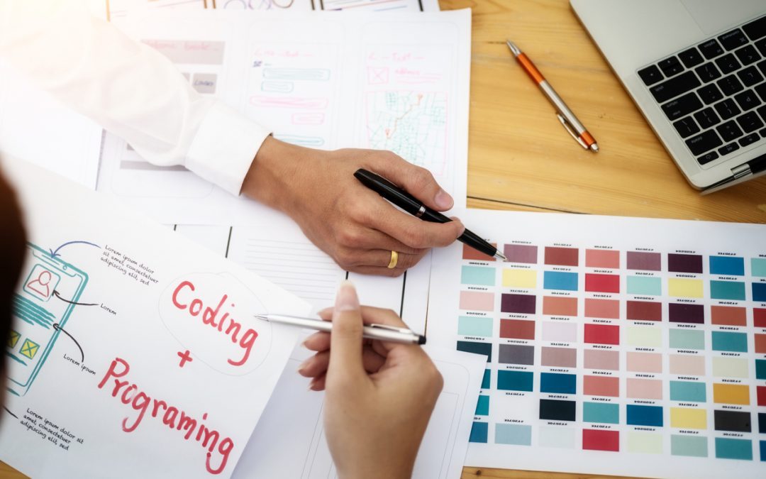 two-people's-hands-working-on-ui-ux-design-papers-on-desk